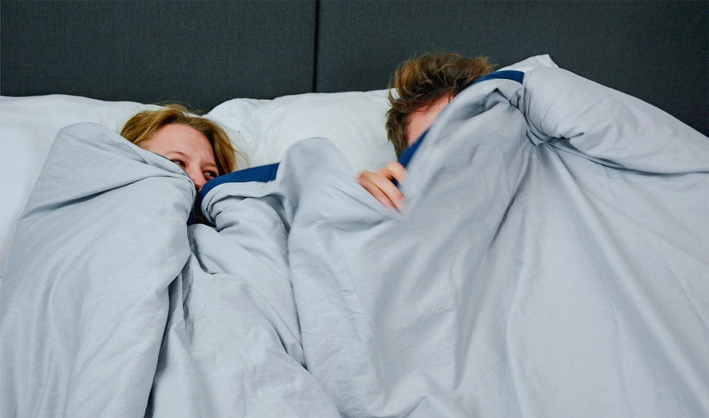 Twee mensen slapen samen in bed onder een grijze verzwaringsdeken.