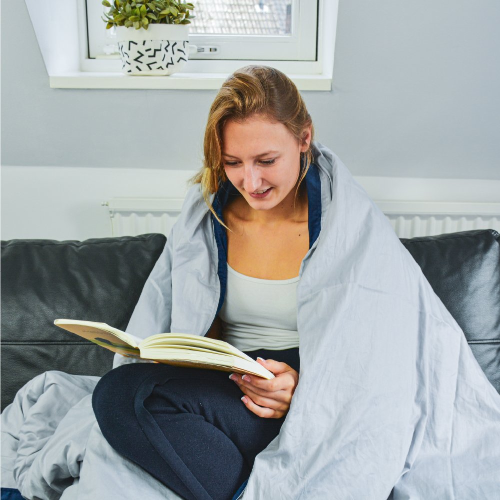 Een vrouw die onder de verzwaarde deken zit van Ella ze is in alle rust aan het genieten van een goed boek