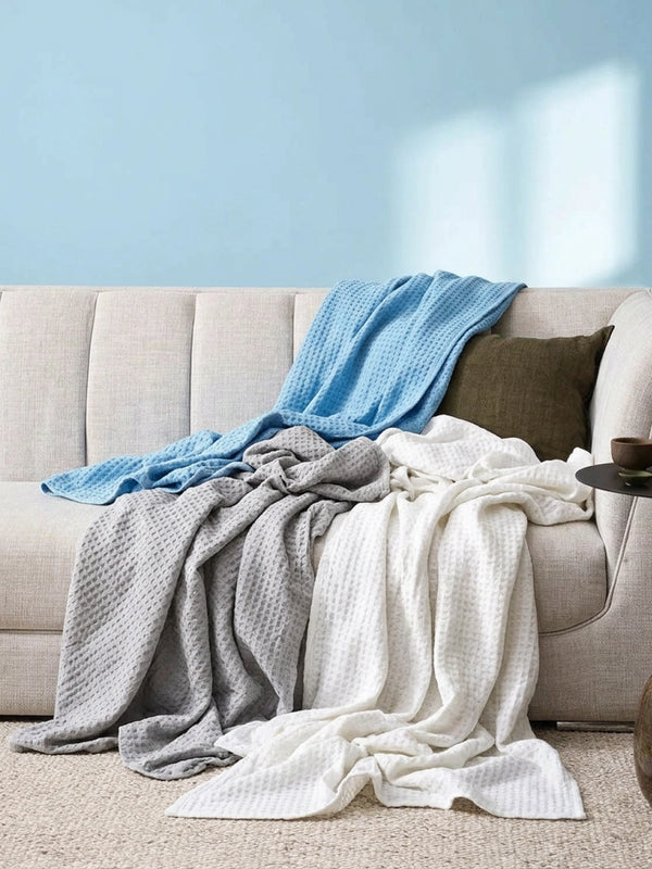 Grijze en blauwe Ella deken stijlvol gedrapeerd op een bed.