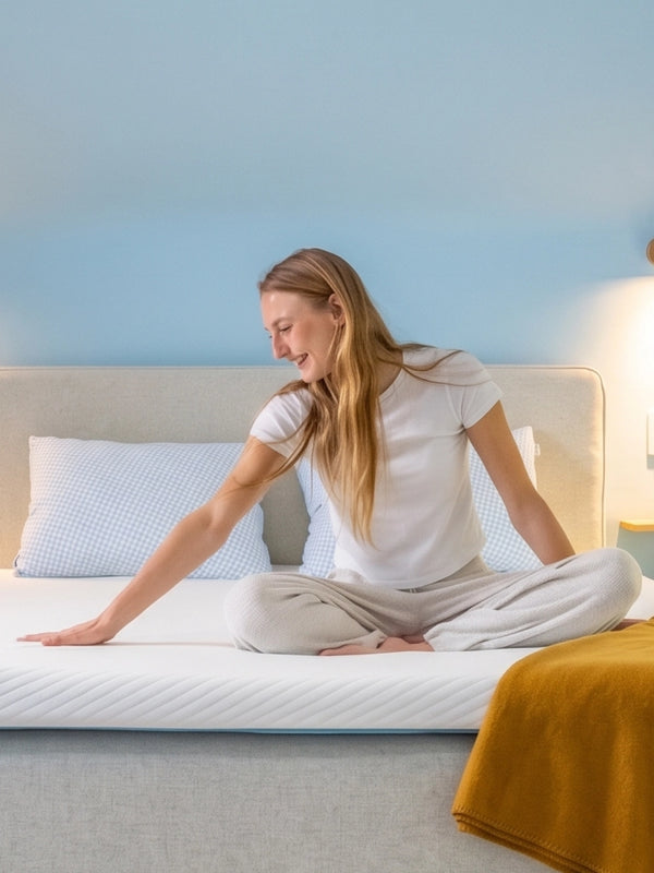Vrouw maakt een bed op met een Ella matrastopper en een gele plaid.
