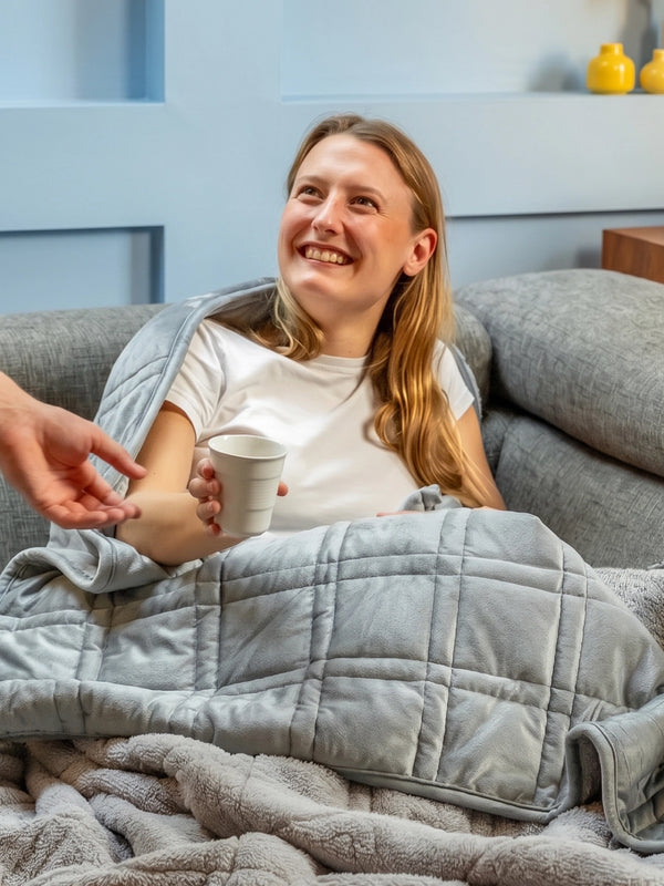 Vrouw ontspant lachend op de bank met een grijze verzwaringsdeken.