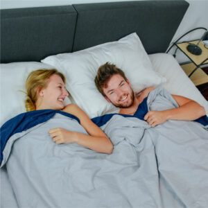 Samen met je partner liggen in bed onder een verzwaringsdeken van Ella, ervaar de rust gevende effecten van een zwaardere deken